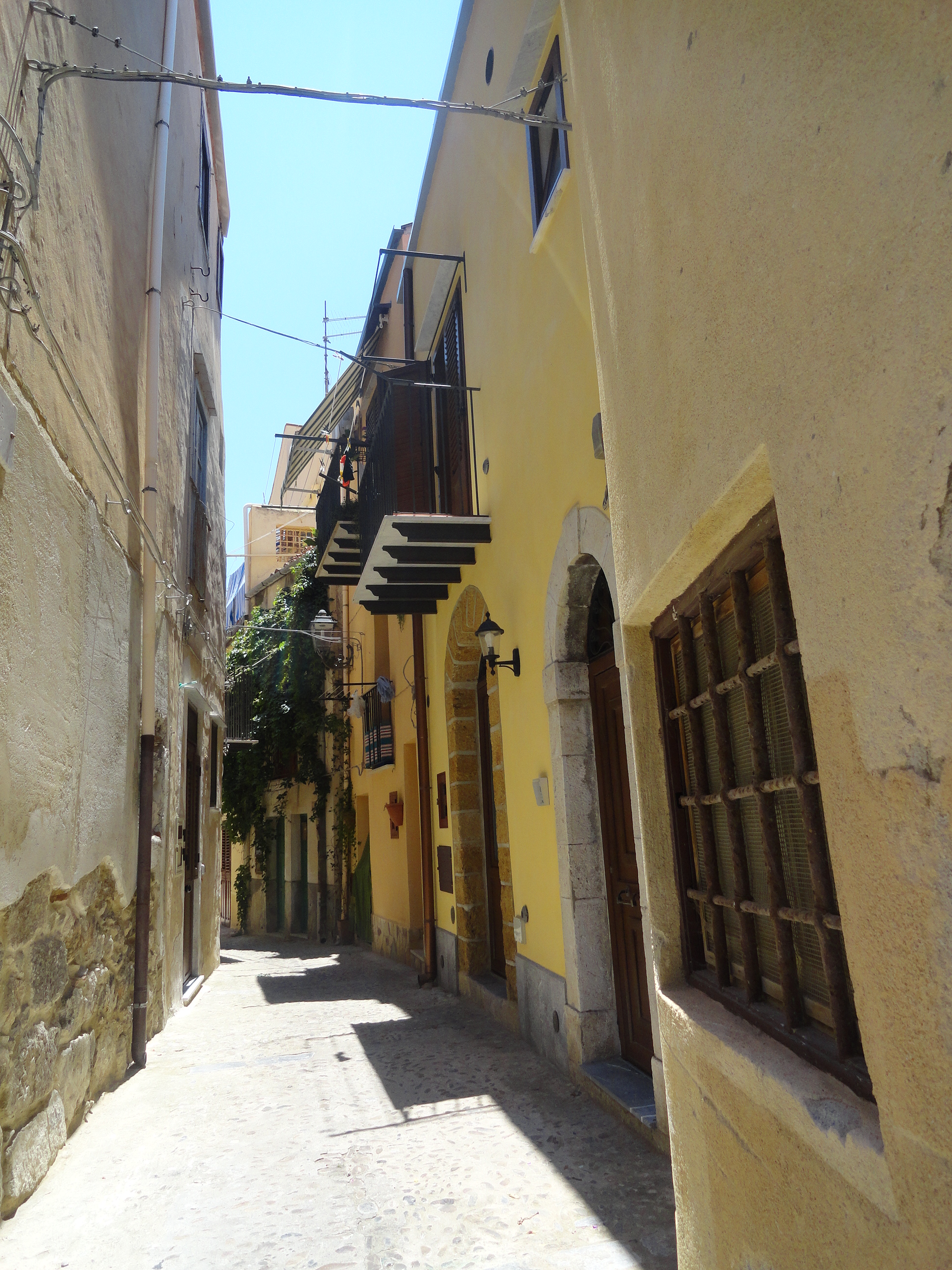 Smal, fargerik gate i Cefalù på Sicilia med varme fasader og tydelig gateforløp mellom bygningene.