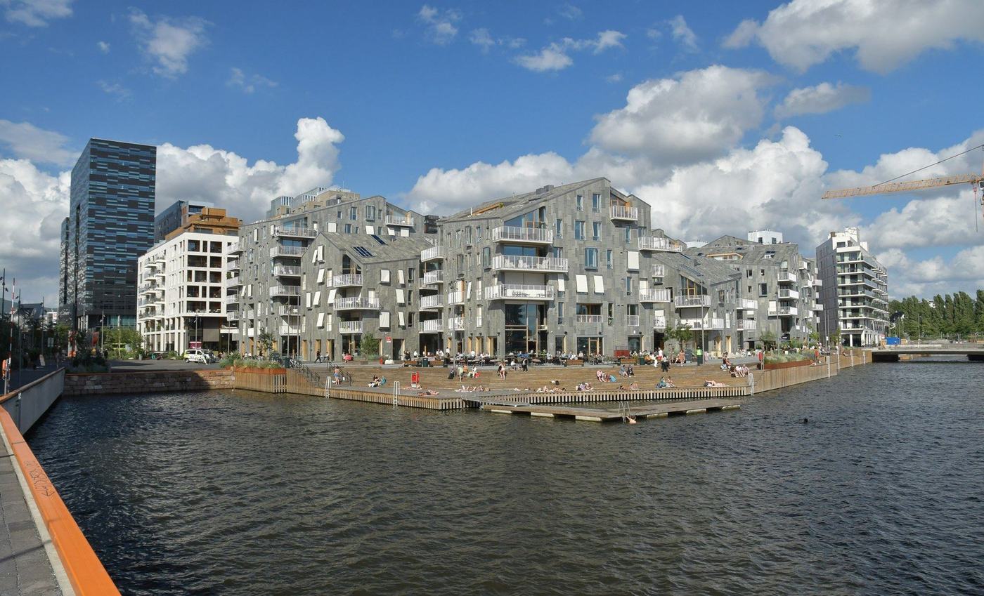 Vannkunsten i Bjørvika i Oslo sett fra kaia ved MUNCH, med grå skiferkledde bygninger langs vannet.